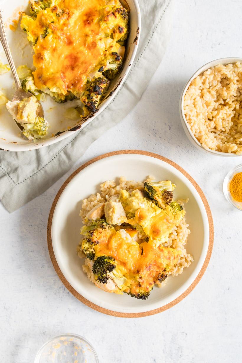 Chicken broccoli divan over rice on a white plate with casserole and other ingredients next to it