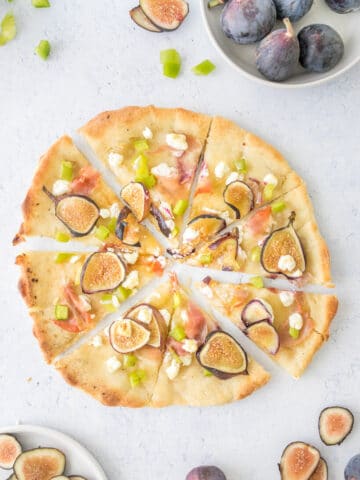 sliced fig and prosciutto pizza with fresh figs and peppers next to it