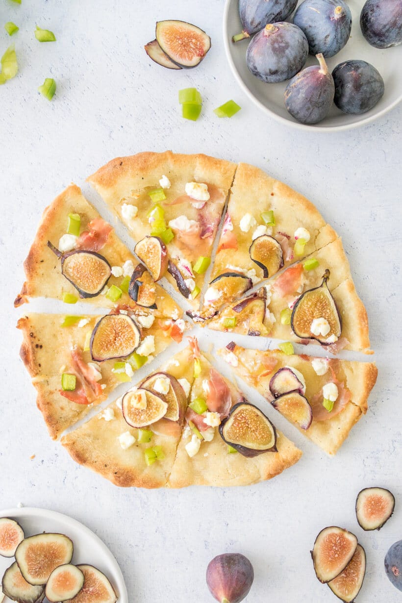 sliced fig and prosciutto pizza with fresh figs and peppers surrounding it