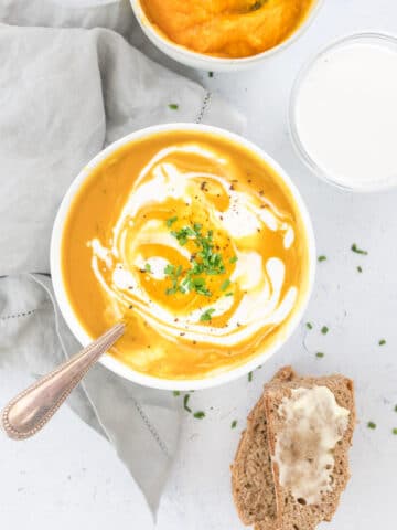 curry pumpkin soup with coconut milk in a white bowl with pumpkin and bread on the side