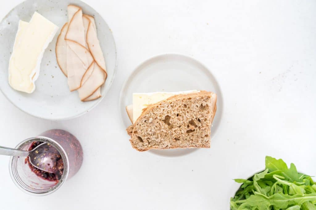 uncooked turkey and brie sandwich on a table with ingredients surrounding it