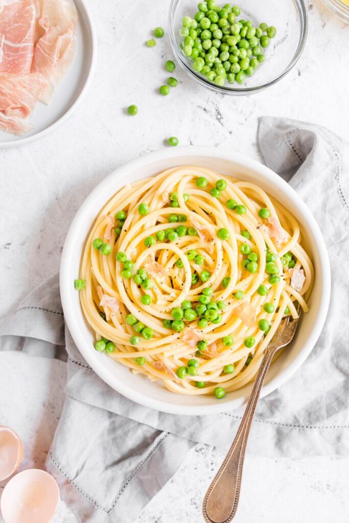 Healthy carbonara in a white bowl with ingredients surrounding it