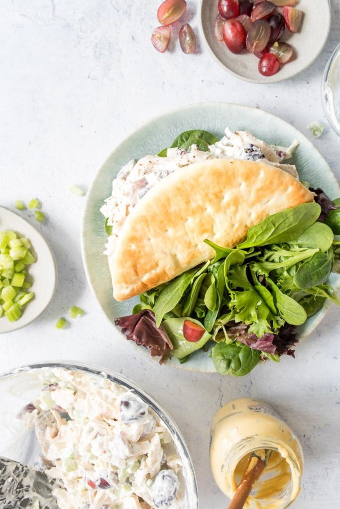 chicken salad pita on a blue plate with salad and ingredients next to it