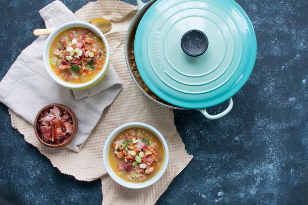 bean and bacon soup in bowls with a teal dutch oven