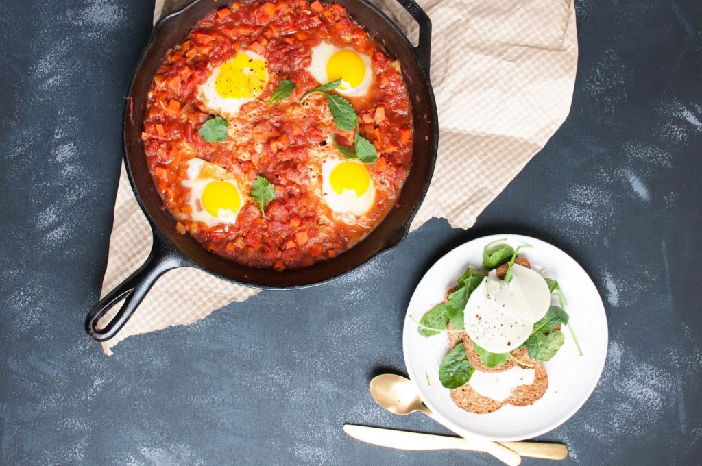 shakshuka in a cast iron skillet and toast with cheese on a table