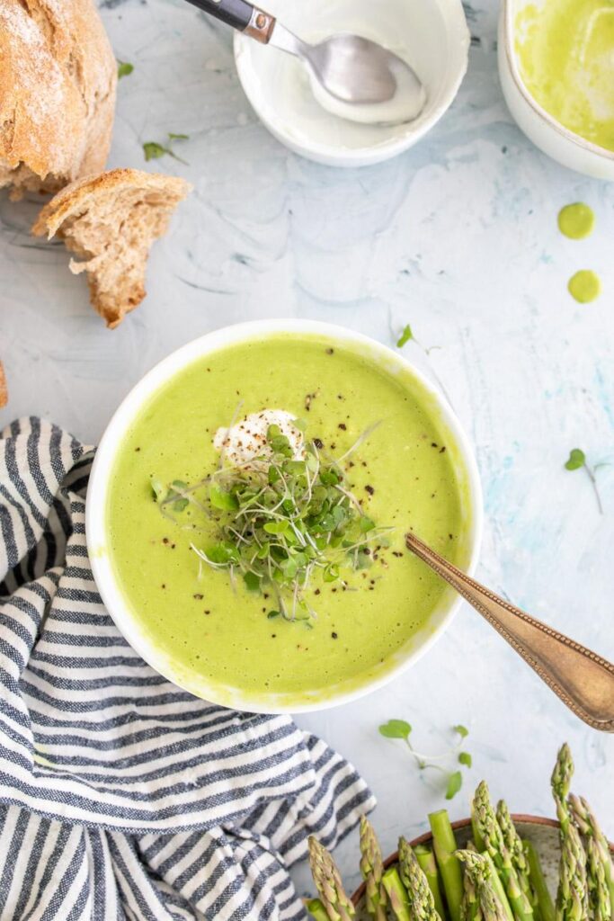 creamy asparagus soup in a white bowl with bread on the side