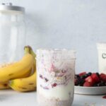 three glass mason jars in a row with oats, yogurt, and fruit on top