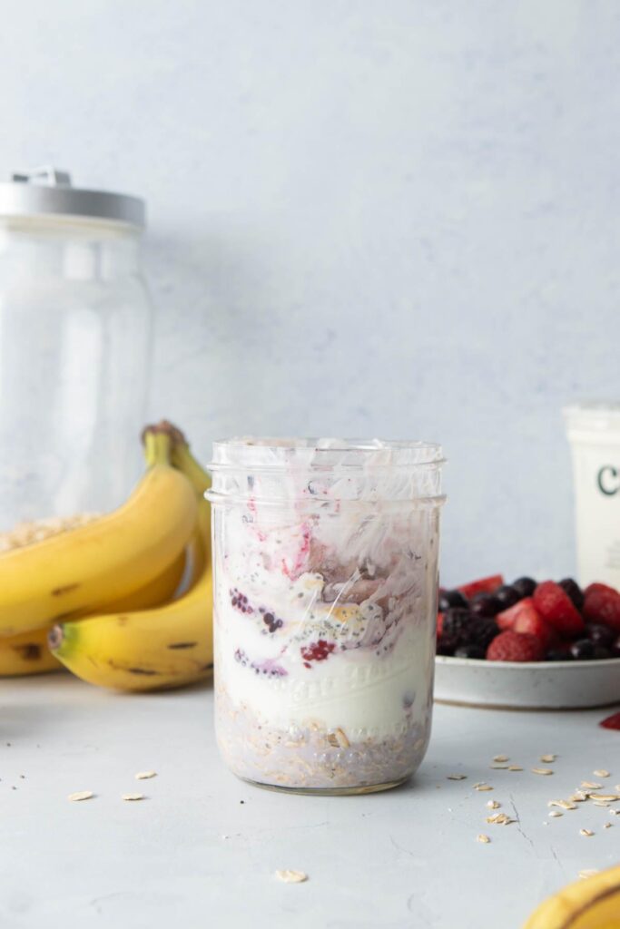 three glass mason jars in a row with oats, yogurt, and fruit on top