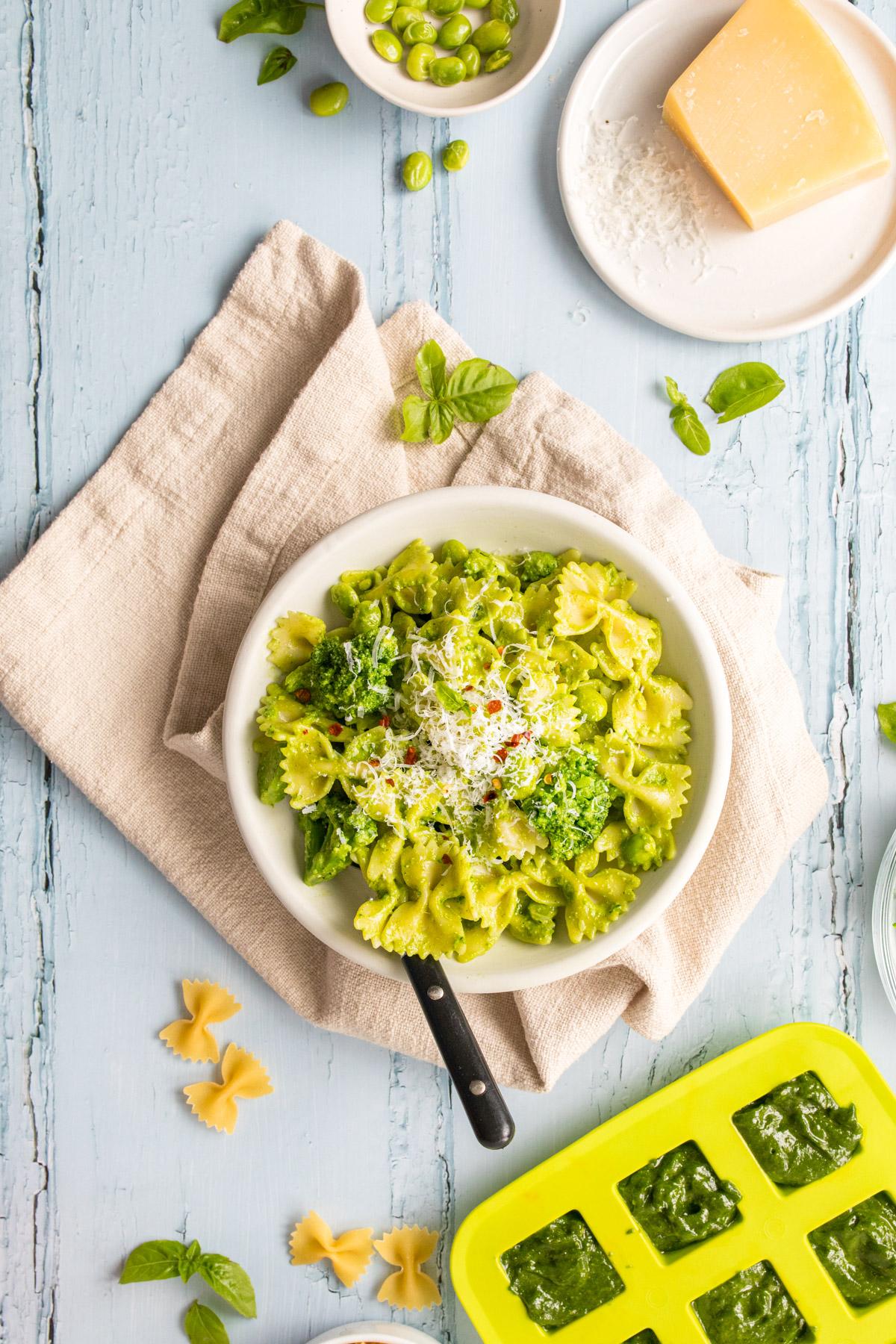 bowtie pasta with pesto in a white bowl with ingredients on table