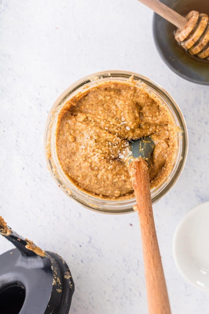 honey almond butter in a glass jar with a spatula in it