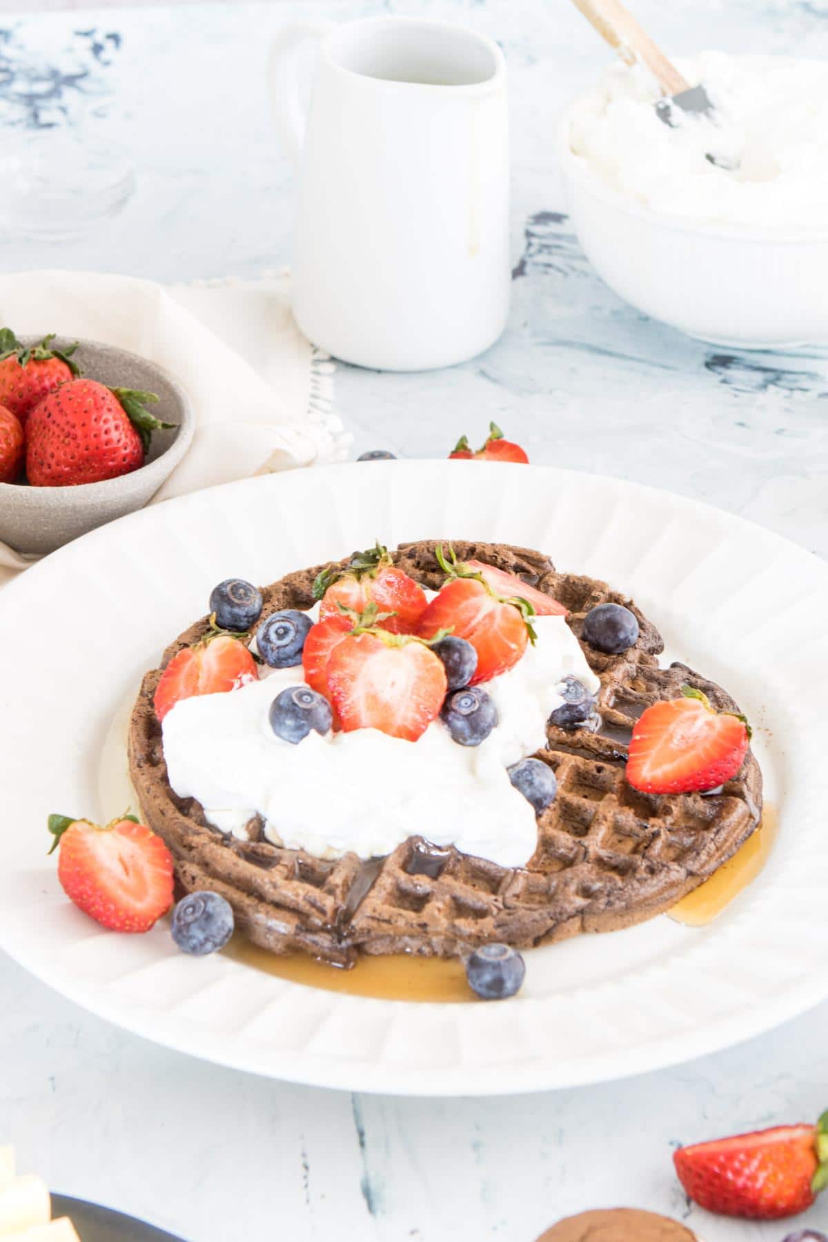 dark chocolate waffle with whipped cream, strawberries, and blueberries on a white plate