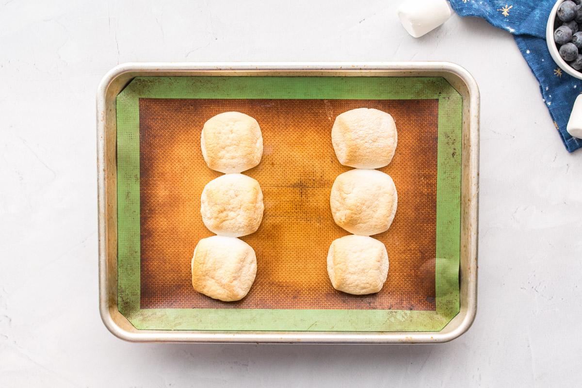 six cooked marshmallows on cookie sheet