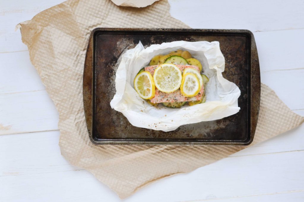 salmon with lemon slices in parchment paper on baking sheet
