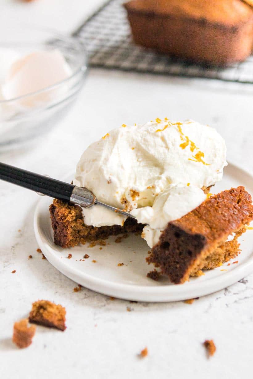 Cut slice of gingerbread pound cake with whipped cream and orange rind with cake in background