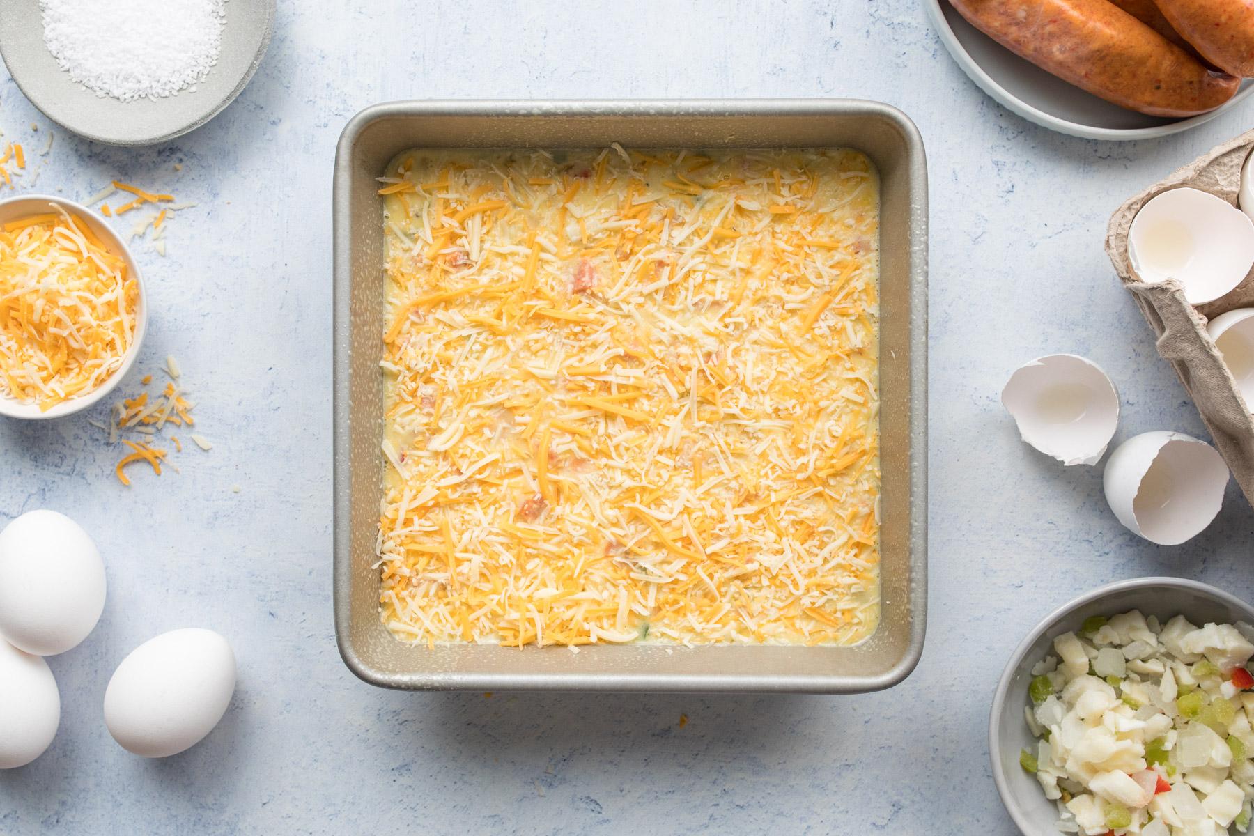 egg casserole ingredients in glass baking pan next to an empty cast iron skillet