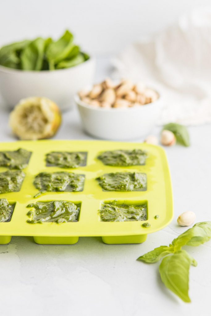 green ice tray with pistachio pesto in it and ingredients in background