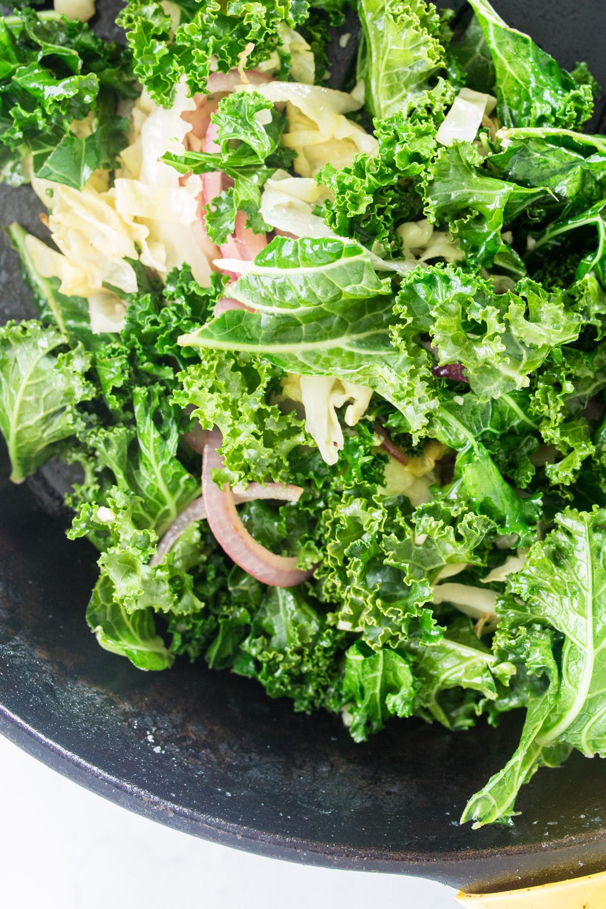 sauteed kale salad with cast iron skillet and bread in the background