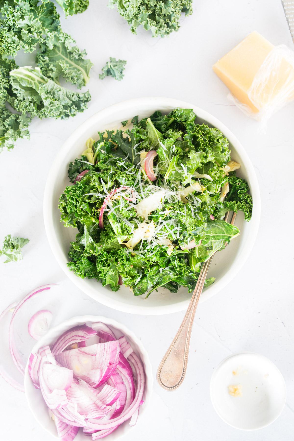 warm kale salad in a bowl with kale, cheese and onions on table