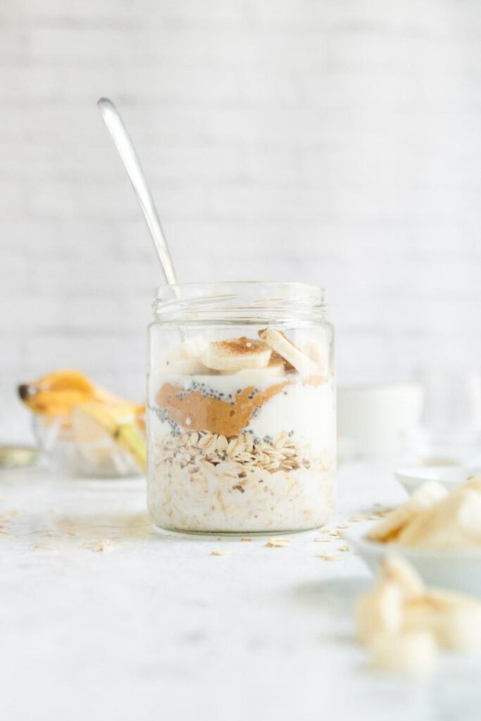 peanut butter overnight oats topped with banana in a glass jar with ingredients in the background