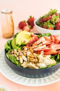 spinach strawberry salad in a blue bowl with ingredients surrounding it