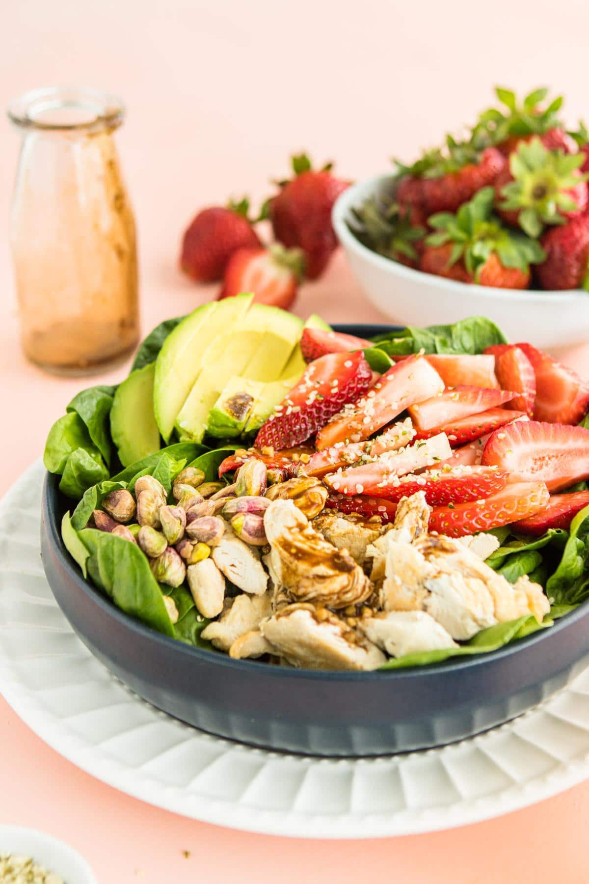 strawberry salad with chicken in a blue bowl with ingredients in the background