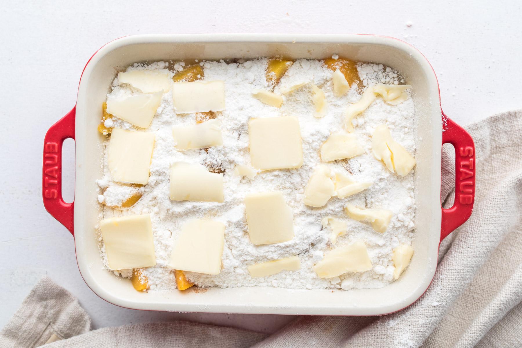 uncooked peach cobbler with butter on top in baking dish