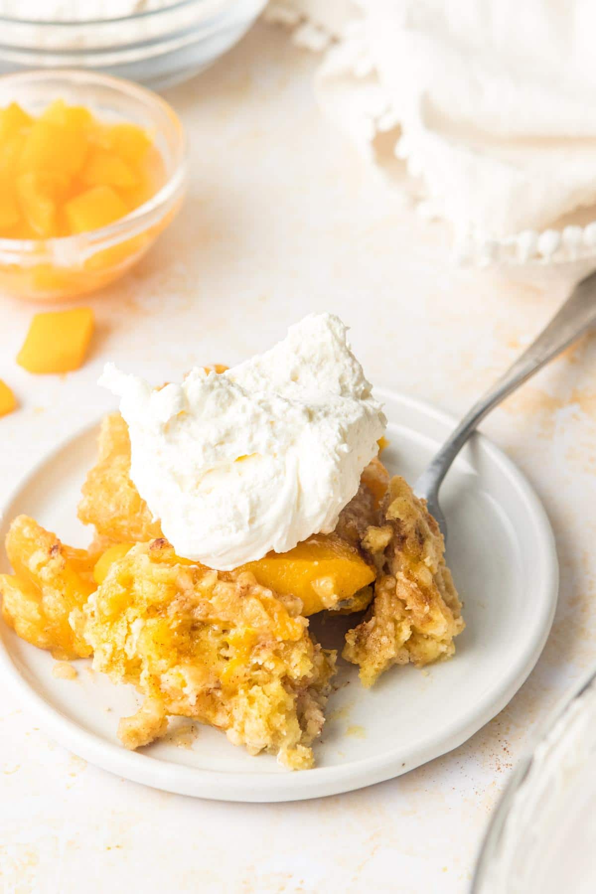 portion of small peach cobbler on plate, with whipped cream