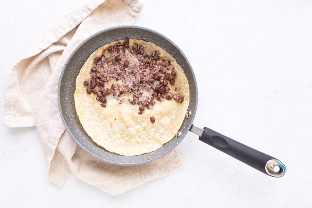 mashed black beans on half of a tortilla in sautee pan