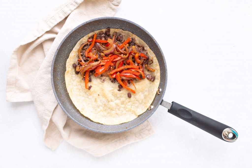 tortilla with black beans, sliced red bell peppers and onions in a skillet