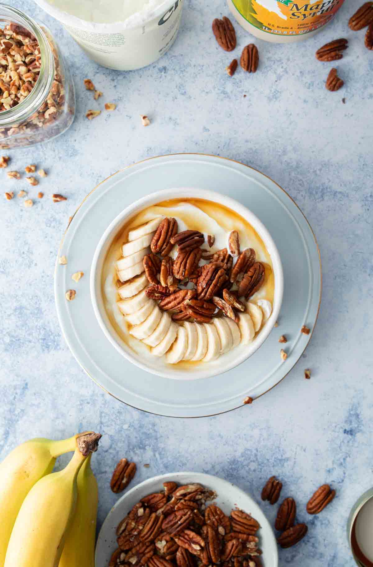 yogurt bowl with banana slices, pecans, and syrup on top