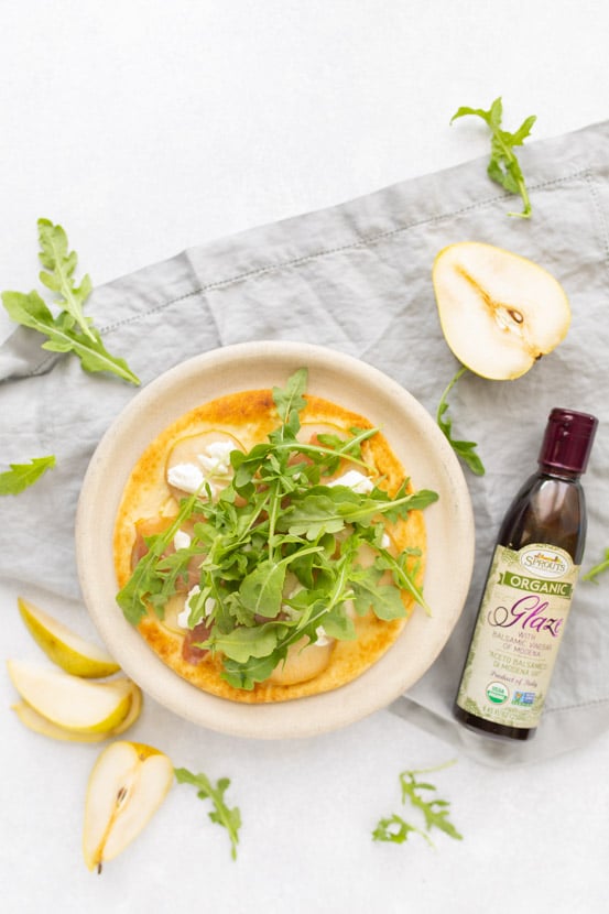 pear prosciutto and arugula flatbread with balsamic glaze and pears on a table with other ingredients on table