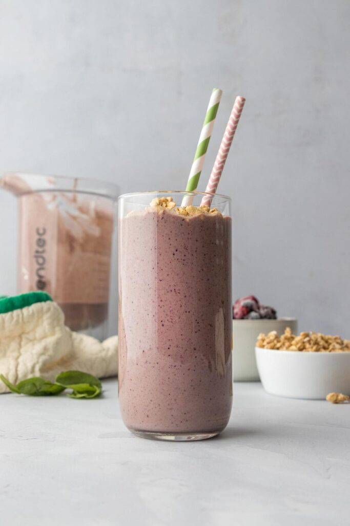 mixed fruit smoothie with granola in tall glass with paper straws