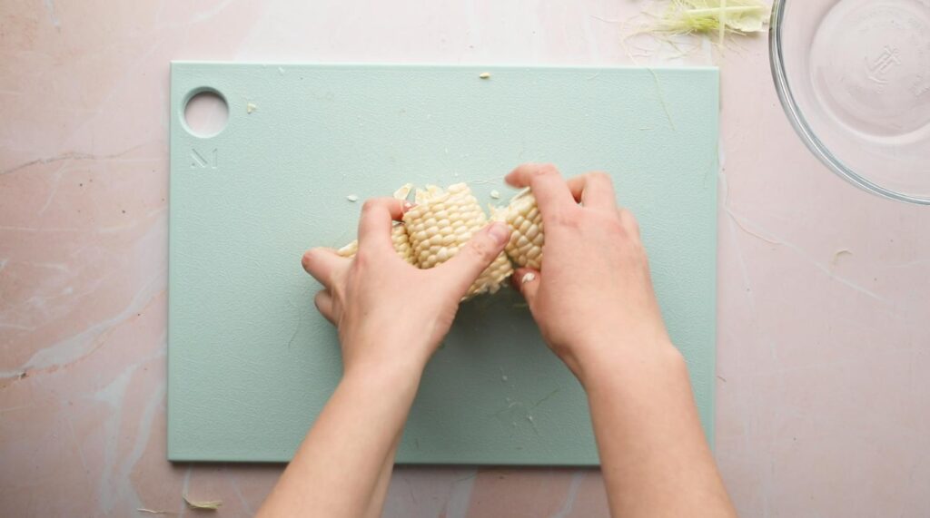 hands holding pieces of an ear of corn on a cutting board