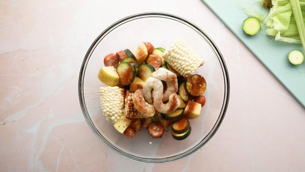 glass bowl of corn, zucchini, sausage, and shrimp with cajun spices on top