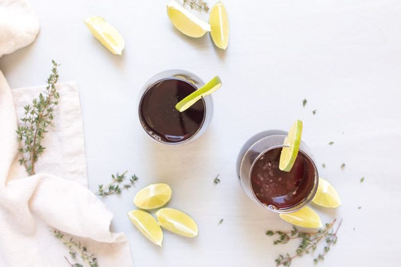 two glasses of tart cherry spritzer on a table with limes and thyme