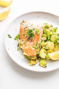 maple mustard salmon and brussels sprouts with a lemon wedge on a white plate