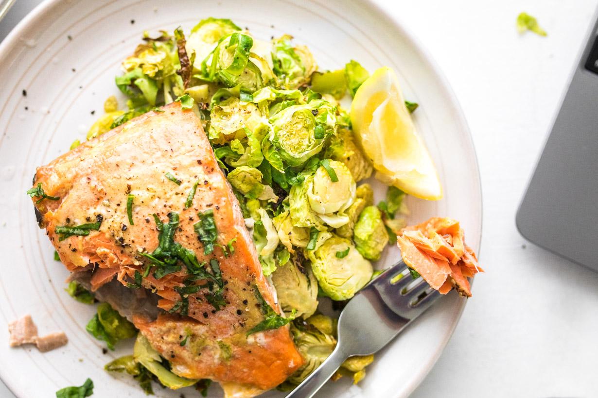 fork with maple mustard salmon on brussels sprouts with a lemon wedge on a white plate