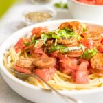 simple pasta in a white bowl with sausage on top and ingredients behind