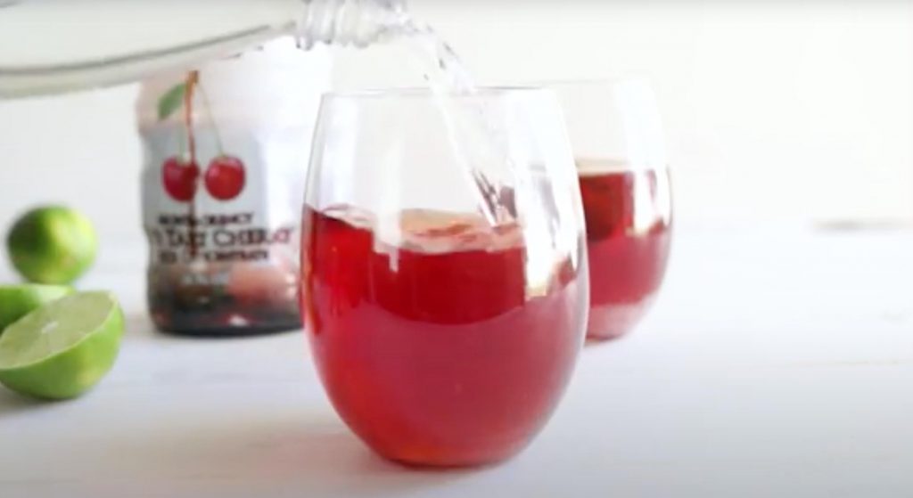 pouring sparkling water into cherry juice in a glass
