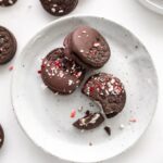 three chocolate dipped oreos with peppermint on a plate and more surrounding it