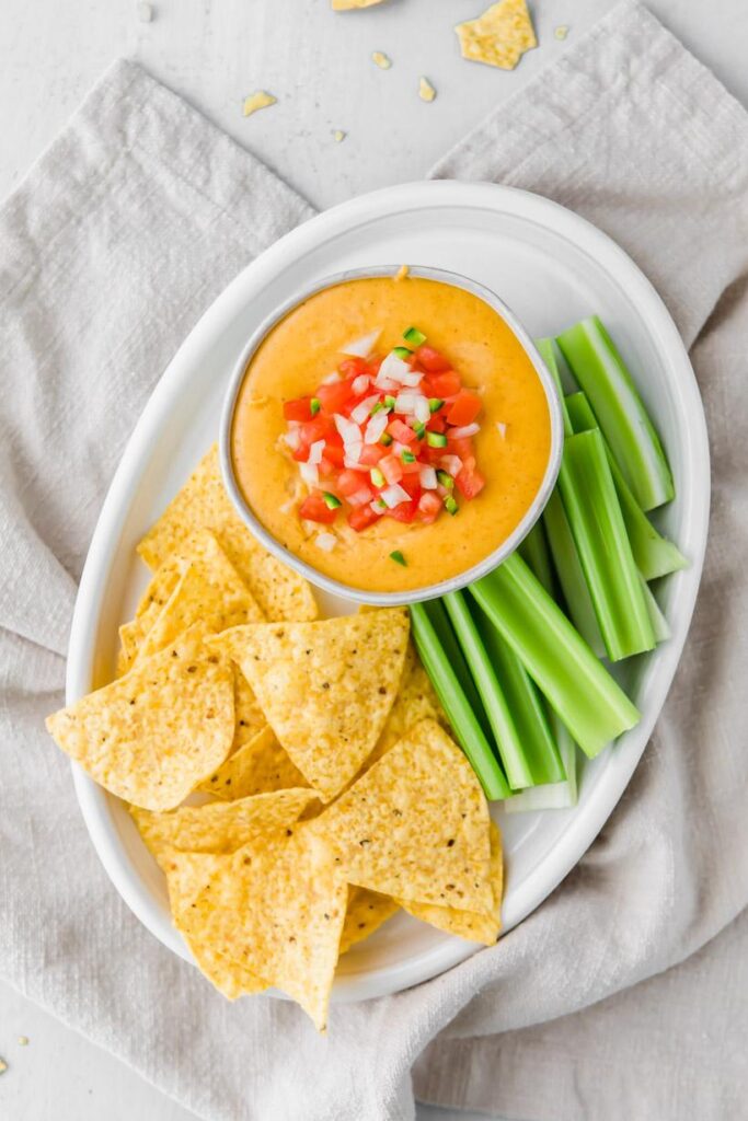 easy queso dip on a plate with salsa on top and chips and celery on the side