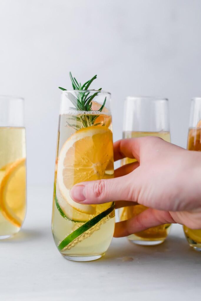 holding an apple mocktail in a stemless champagne glass with citrus and rosemary