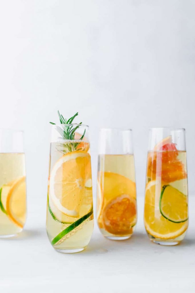 apple mocktails in stemless champagne glasses with citrus and rosemary
