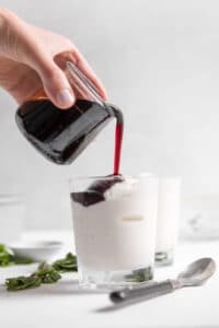 pouring tart cherry sauce onto frozen greek yogurt in a glass