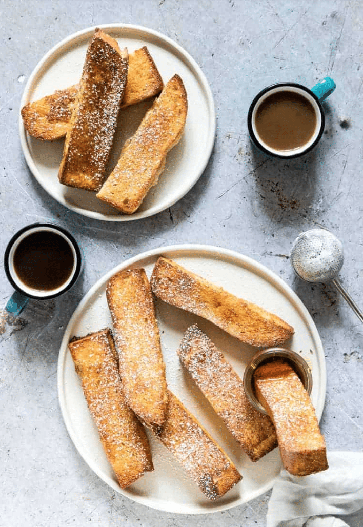 french toast sticks on two plates with mugs on a table
