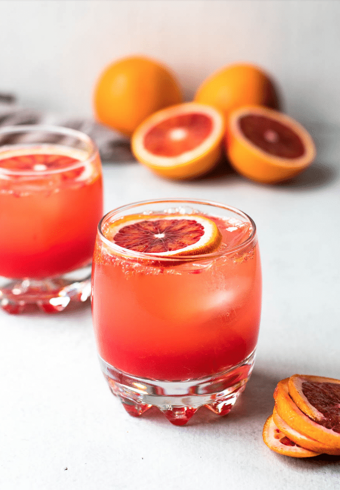 blood orange drink with a slice of blood orange on top with oranges in background