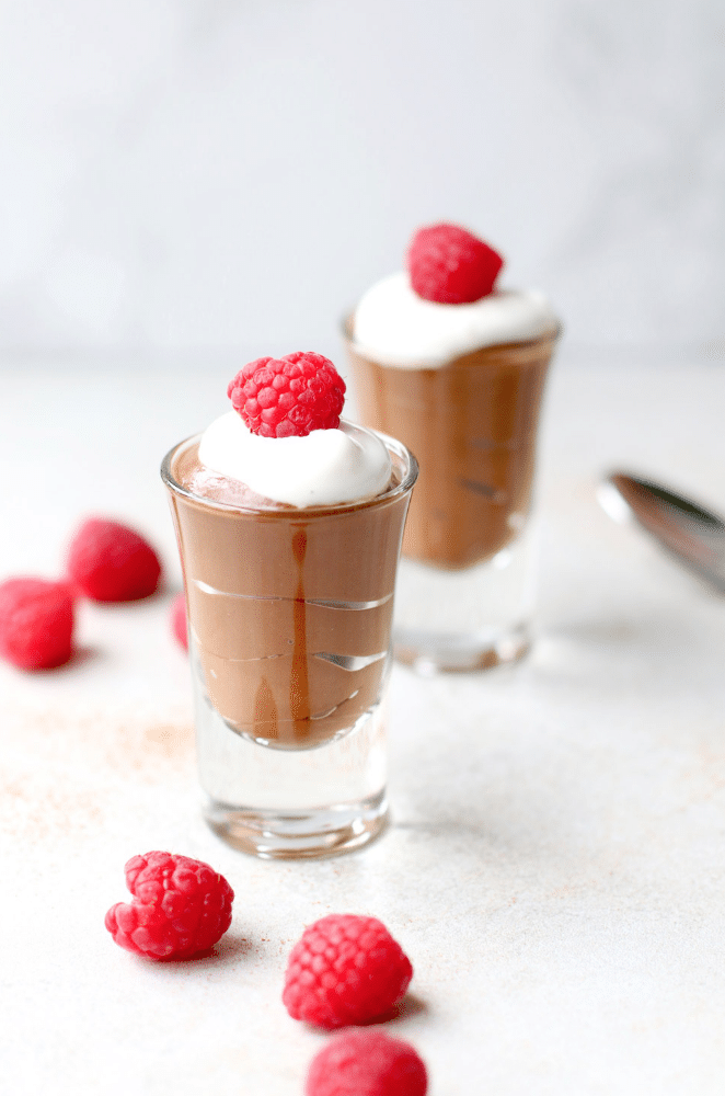 two small glasses with chocolate mousse topped with whipped cream and raspberries