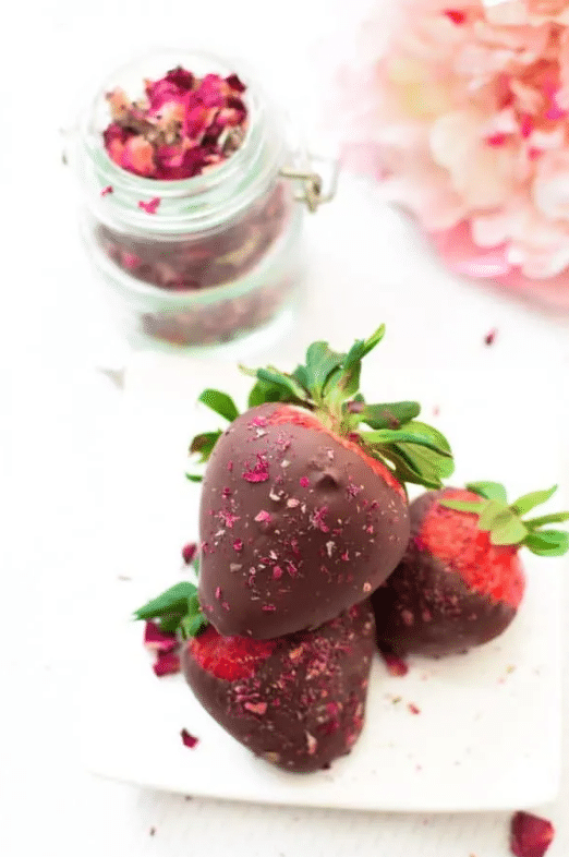 three chocolate covered strawberries with rose petals on top