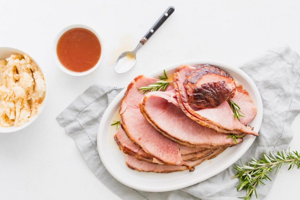 maple glazed ham on a plate with more glaze in a dish