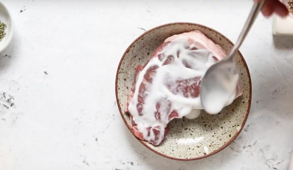 spoon spreading yogurt on uncooked lamb steak